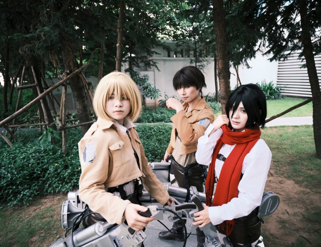 Group of three cosplayers dressed as anime characters in an outdoor setting.